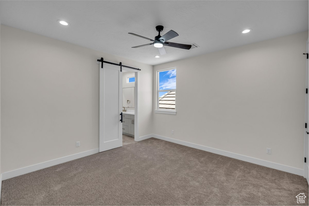 Unfurnished bedroom with a barn door, light carpet, recessed lighting, ensuite bathroom, and ceiling fan