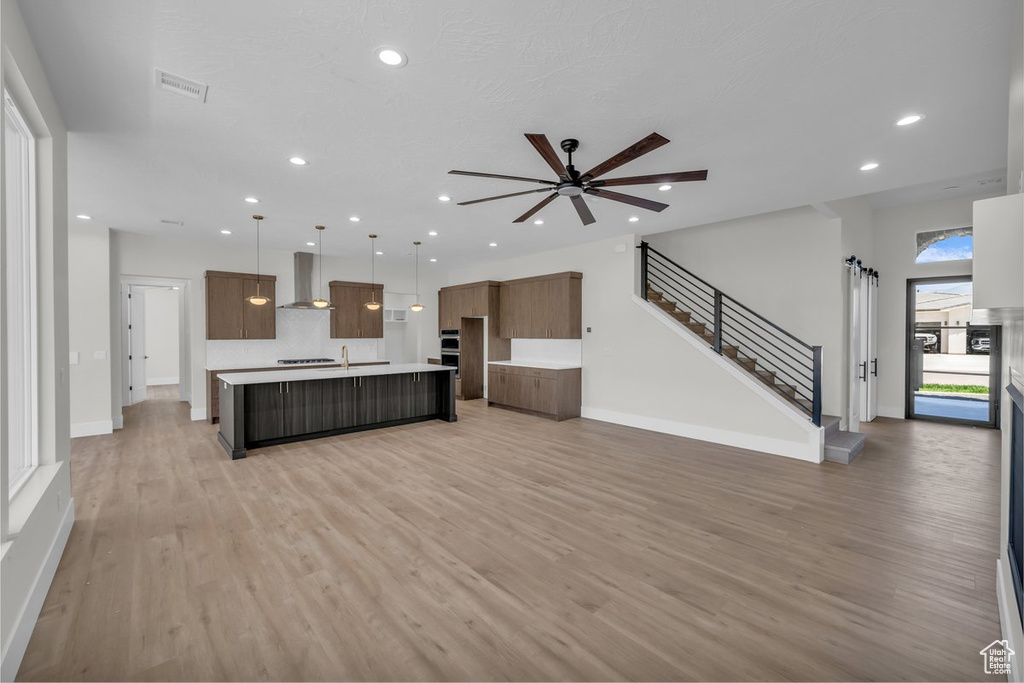 Unfurnished living room with light wood finished floors, recessed lighting, a ceiling fan, and stairs