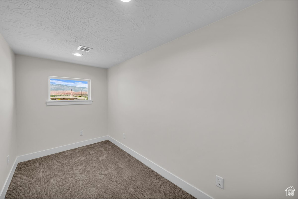 Empty room featuring dark carpet, a textured ceiling, and recessed lighting
