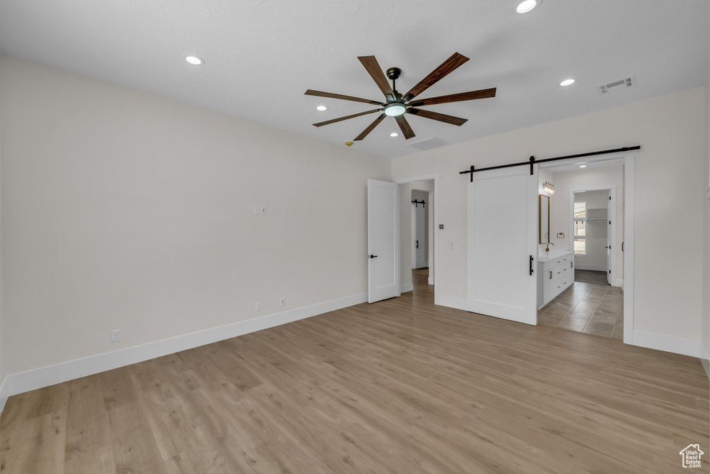 Empty room featuring a barn door, a ceiling fan, light wood finished floors, and recessed lighting