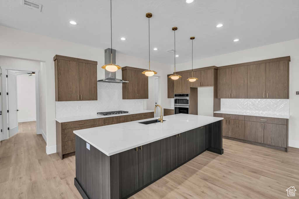 Kitchen with wall chimney exhaust hood, appliances with stainless steel finishes, decorative backsplash, light wood-type flooring, and recessed lighting