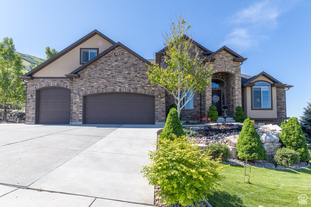 French provincial home with driveway, a garage, a front lawn, stucco siding, and brick siding