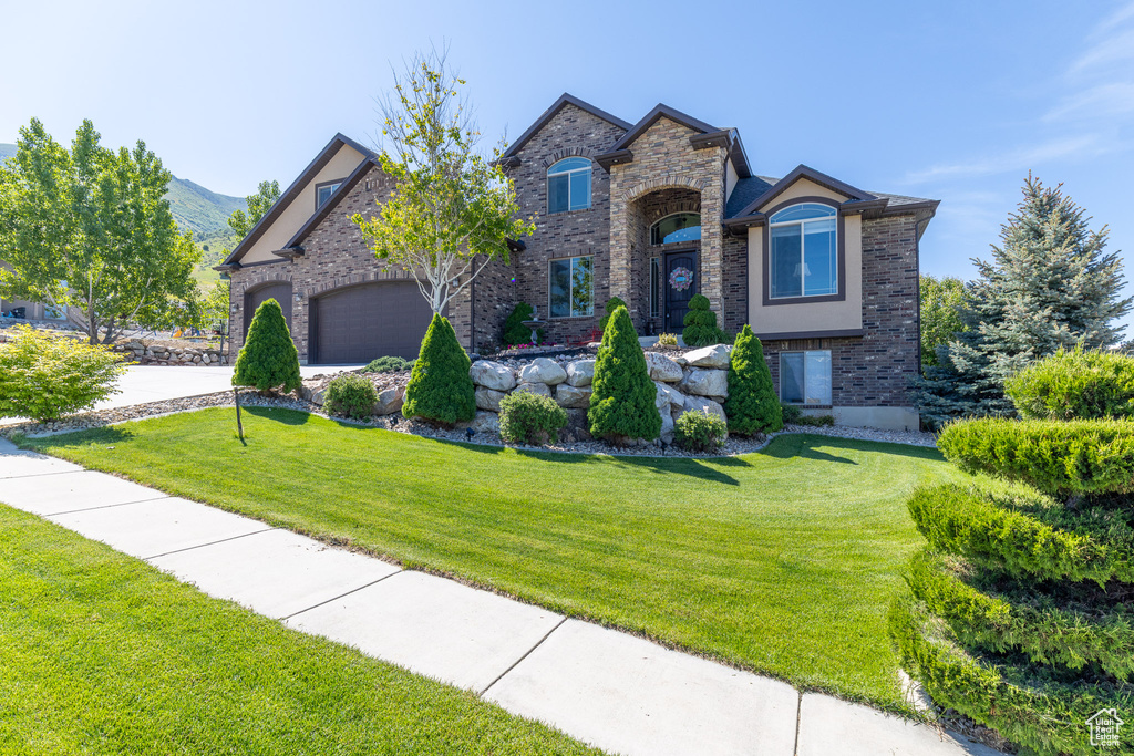 View of front of house with a front yard, brick siding, concrete driveway, and a garage