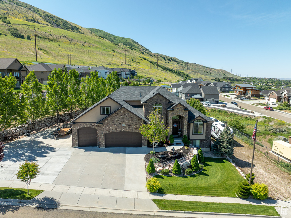 View of front of house featuring stone siding, a residential view, concrete driveway, a mountain view, and an attached garage