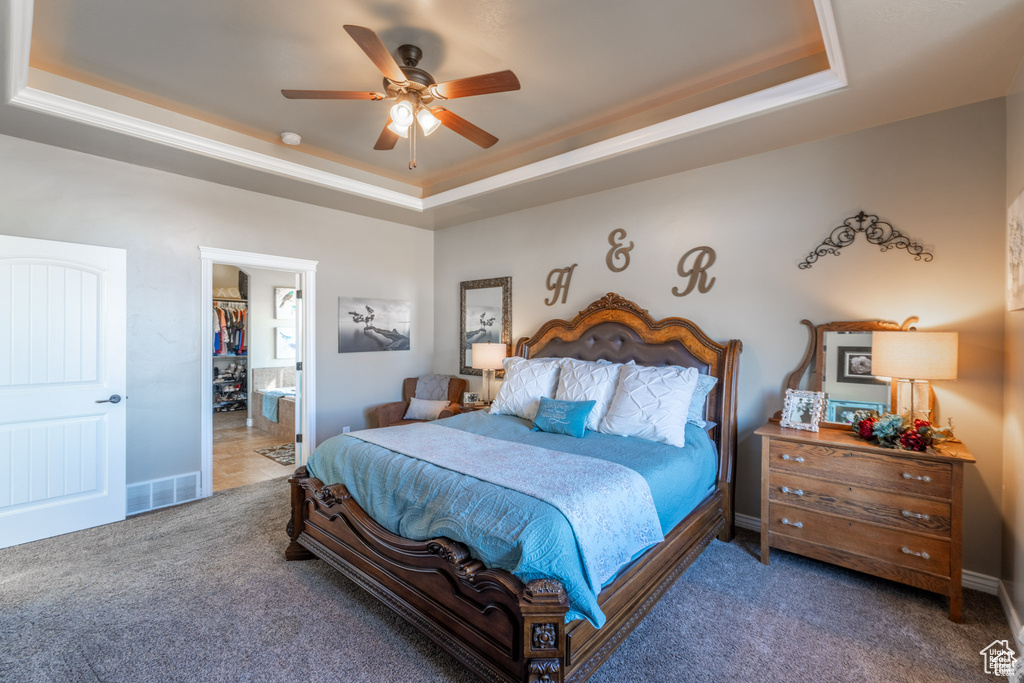 Bedroom with a raised ceiling, carpet floors, ceiling fan, and ensuite bath