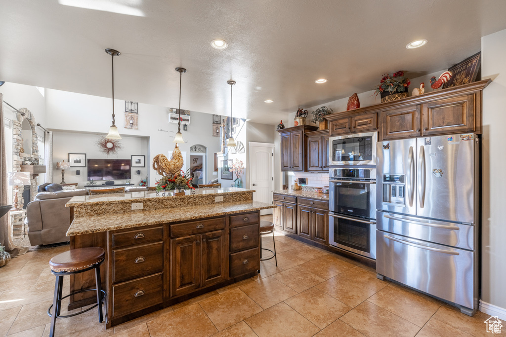 Kitchen featuring stainless steel appliances, a kitchen breakfast bar, open floor plan, dark brown cabinetry, and a center island