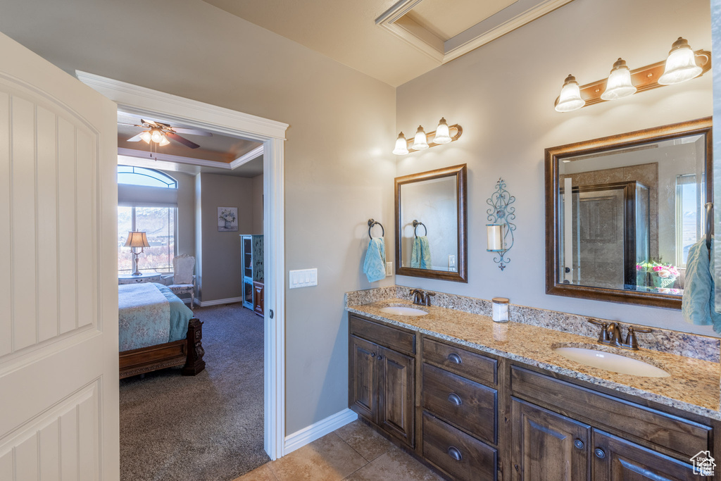 Ensuite bathroom with double vanity, a ceiling fan, crown molding, and a raised ceiling