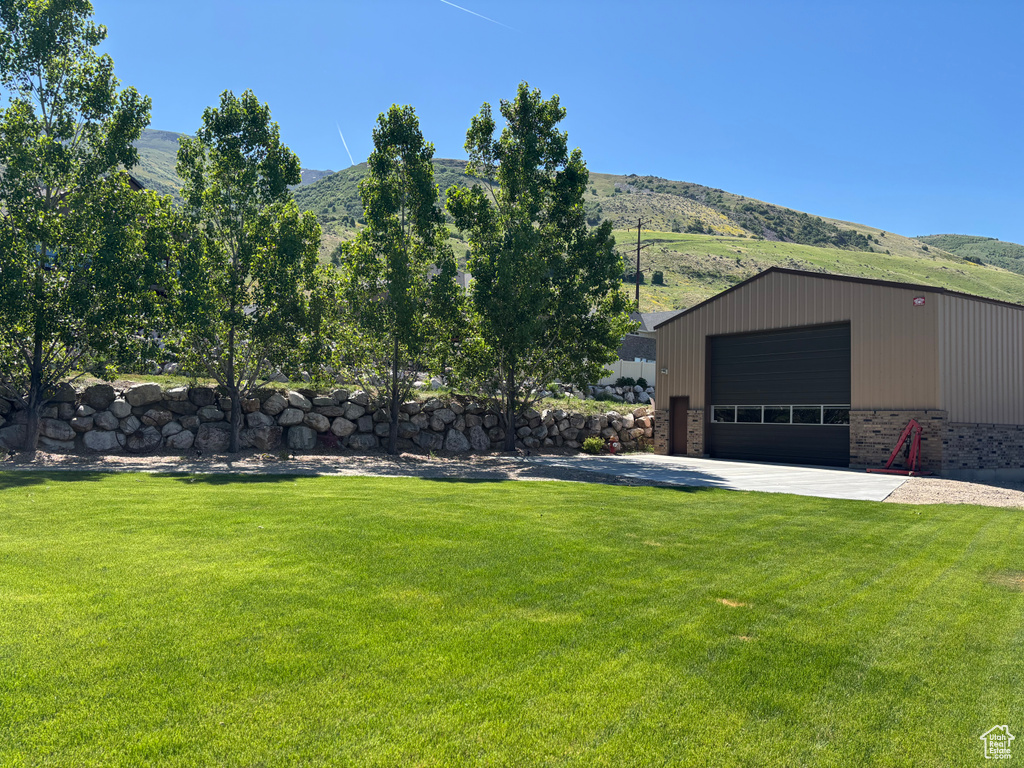 View of green lawn featuring a mountain view, an outdoor structure, and a detached garage
