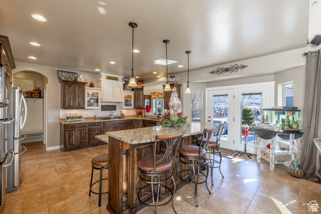 Kitchen featuring a breakfast bar, light stone countertops, tasteful backsplash, stainless steel gas stovetop, and a kitchen island