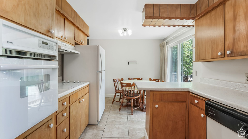 Kitchen featuring white appliances, under cabinet range hood, light countertops, a peninsula, and brown cabinetry