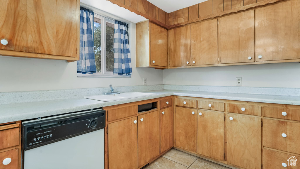 Kitchen with white dishwasher, light countertops, light tile patterned flooring, and brown cabinetry