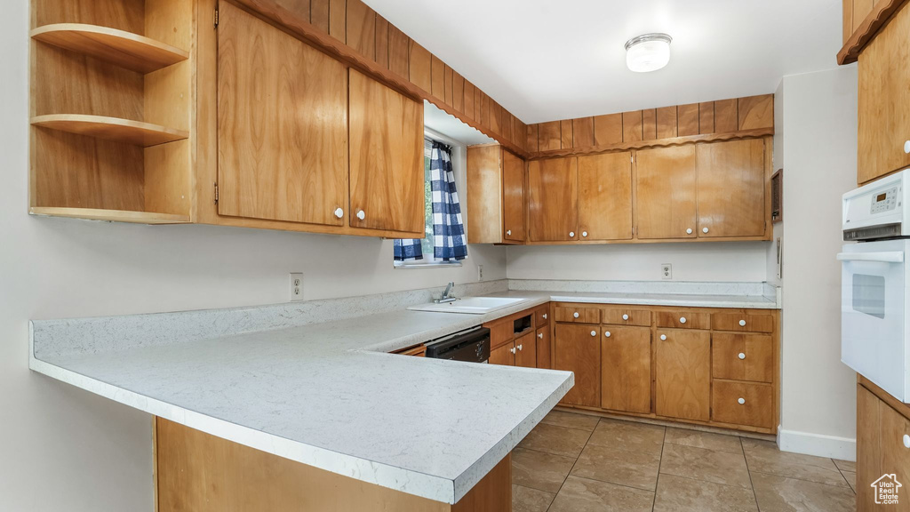 Kitchen with white oven, light countertops, brown cabinets, a peninsula, and black dishwasher
