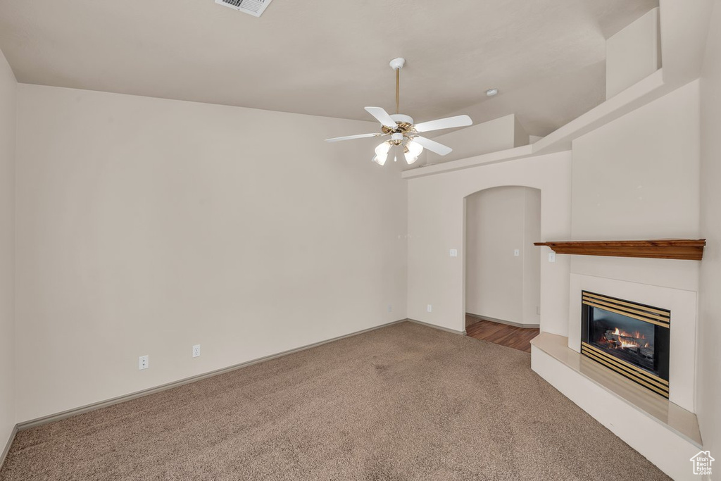 Unfurnished living room featuring carpet flooring, a ceiling fan, arched walkways, and a glass covered fireplace