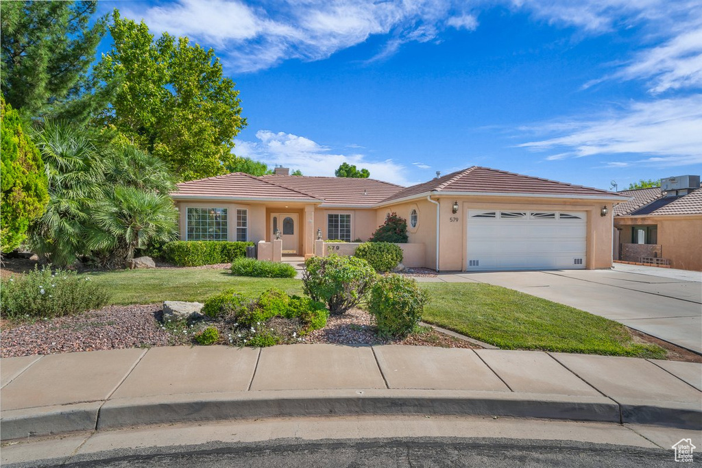 Single story home with a tile roof, an attached garage, stucco siding, and a front lawn