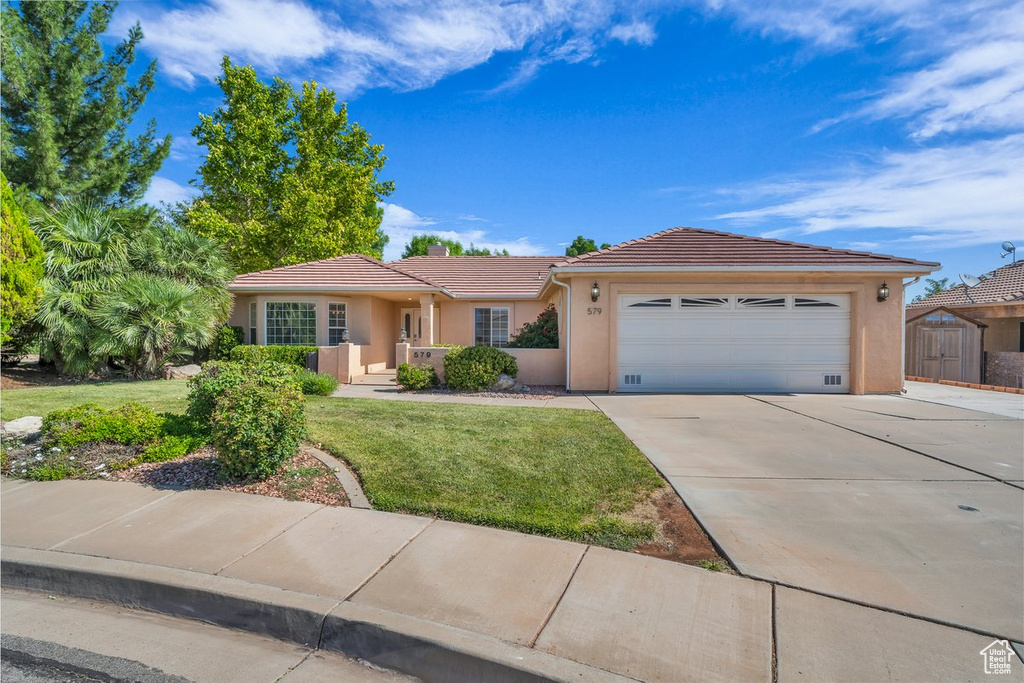 Single story home featuring a tile roof, concrete driveway, an attached garage, stucco siding, and a front lawn