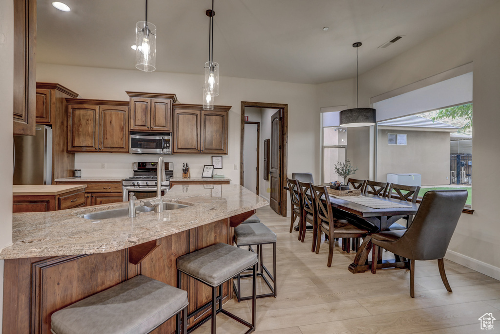 Kitchen with appliances with stainless steel finishes, a breakfast bar, decorative light fixtures, light stone counters, and recessed lighting