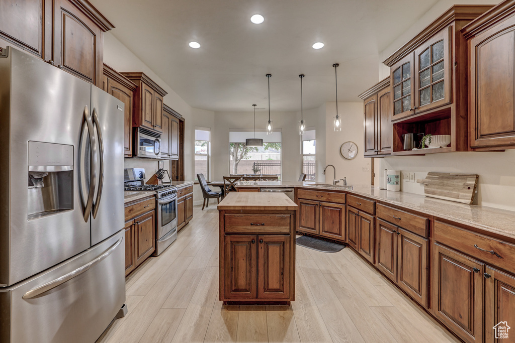 Kitchen with stainless steel appliances, a peninsula, recessed lighting, pendant lighting, and glass insert cabinets