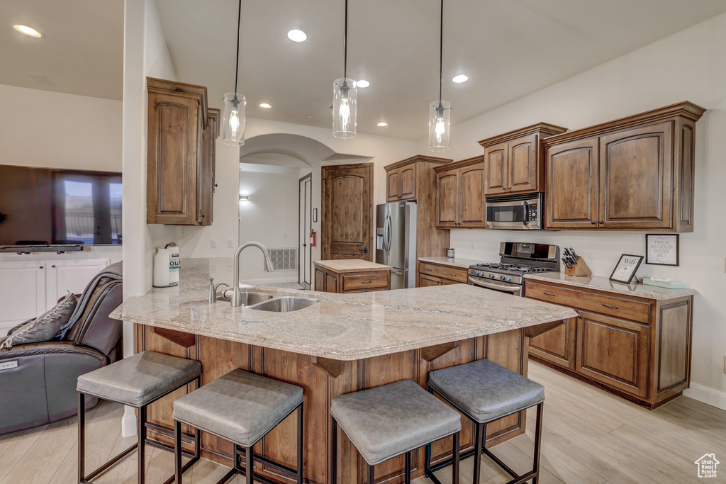 Kitchen featuring appliances with stainless steel finishes, a peninsula, light wood finished floors, a kitchen breakfast bar, and arched walkways
