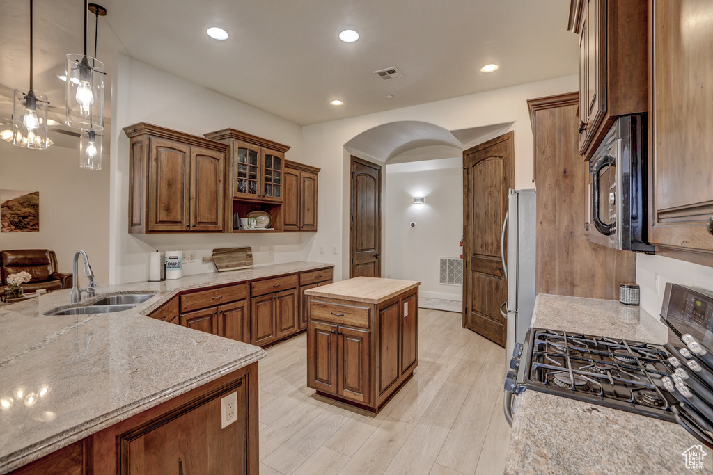 Kitchen with appliances with stainless steel finishes, arched walkways, light wood finished floors, light stone counters, and open shelves