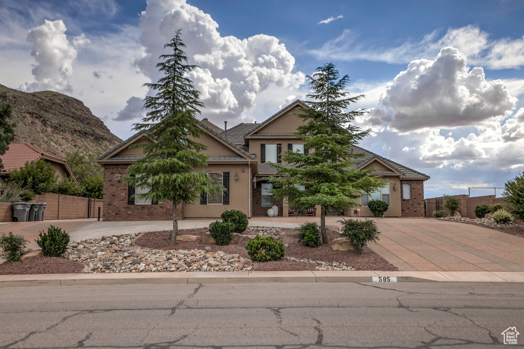 View of property hidden behind natural elements featuring concrete driveway and brick siding