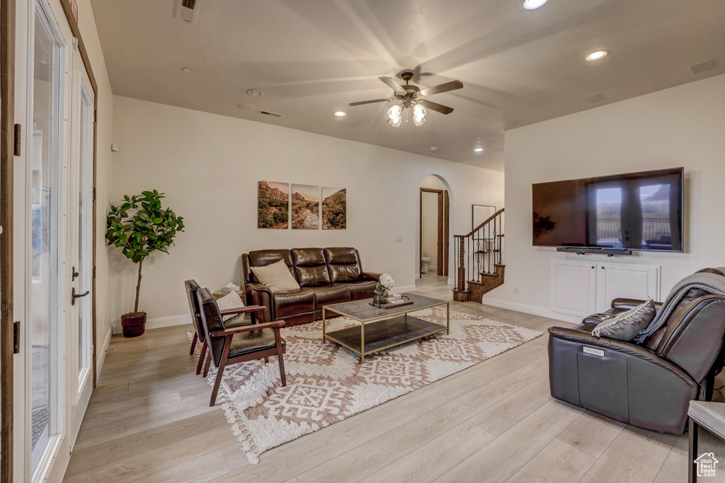 Living room with arched walkways, light wood-style flooring, recessed lighting, stairs, and a ceiling fan