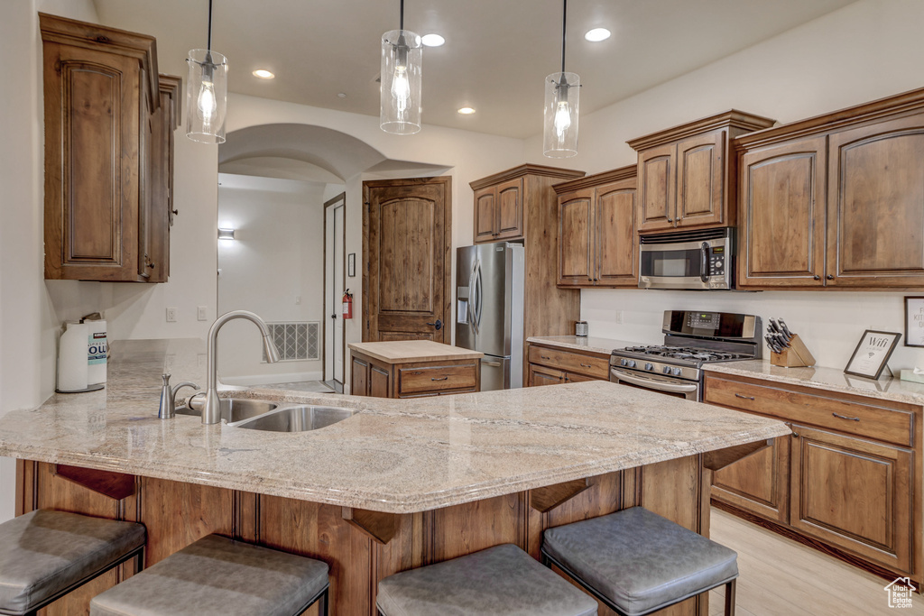Kitchen featuring appliances with stainless steel finishes, a peninsula, a breakfast bar, light stone counters, and recessed lighting