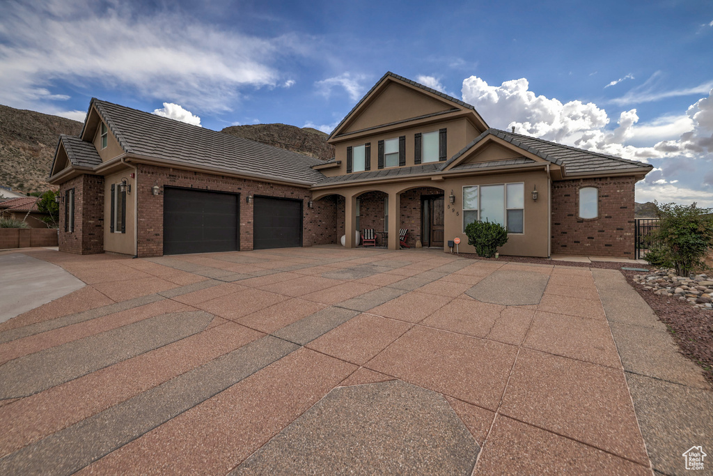 Traditional-style home featuring brick siding, concrete driveway, a garage, a porch, and a tiled roof