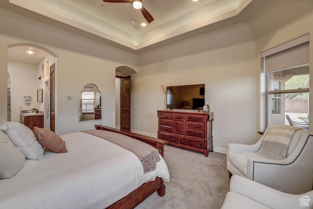 Carpeted bedroom with arched walkways, recessed lighting, ceiling fan, a tray ceiling, and connected bathroom