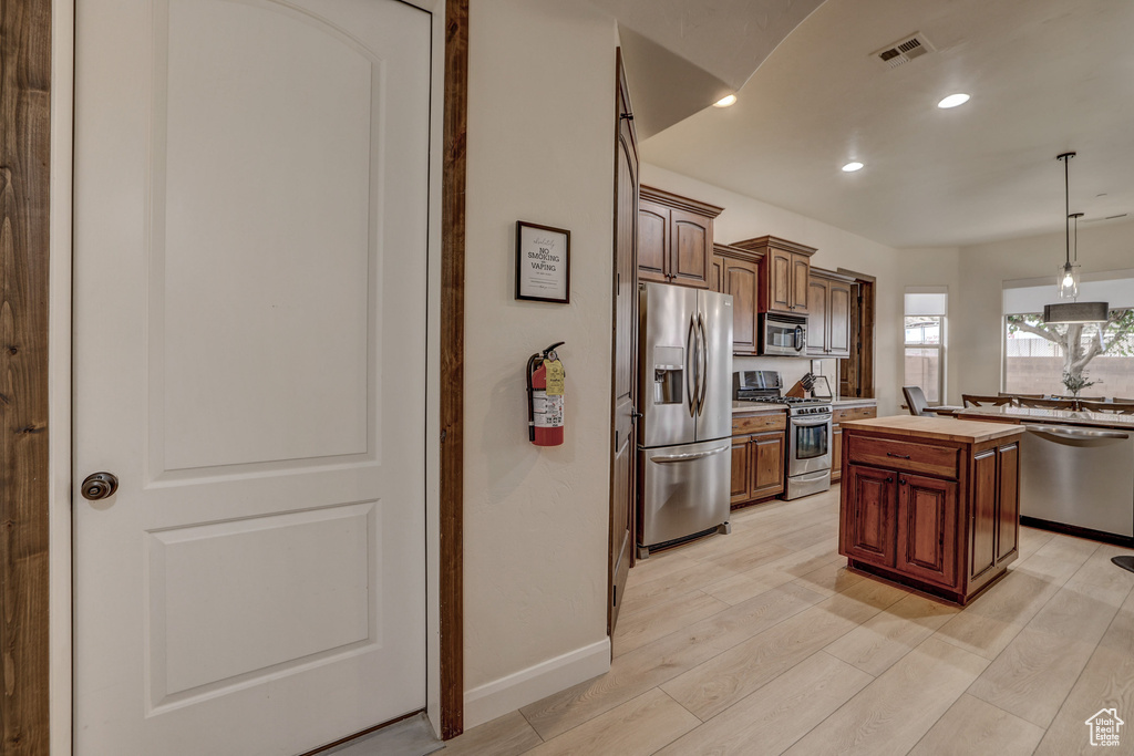 Kitchen featuring appliances with stainless steel finishes, a center island, decorative light fixtures, butcher block counters, and light wood-style floors