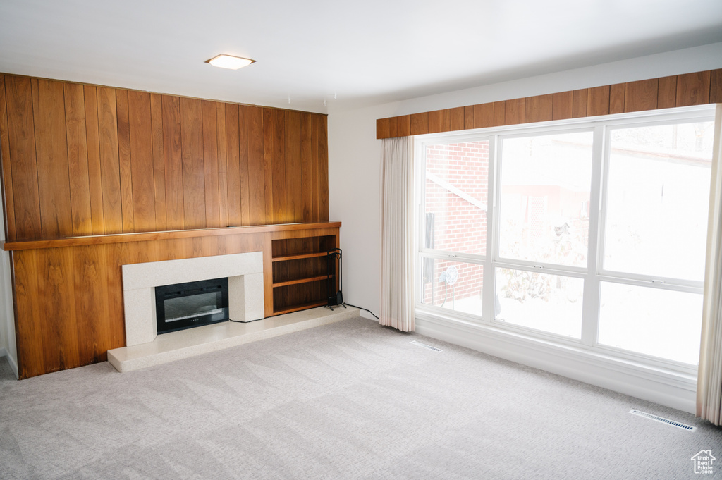 Unfurnished living room with carpet flooring, wood walls, and a glass covered fireplace