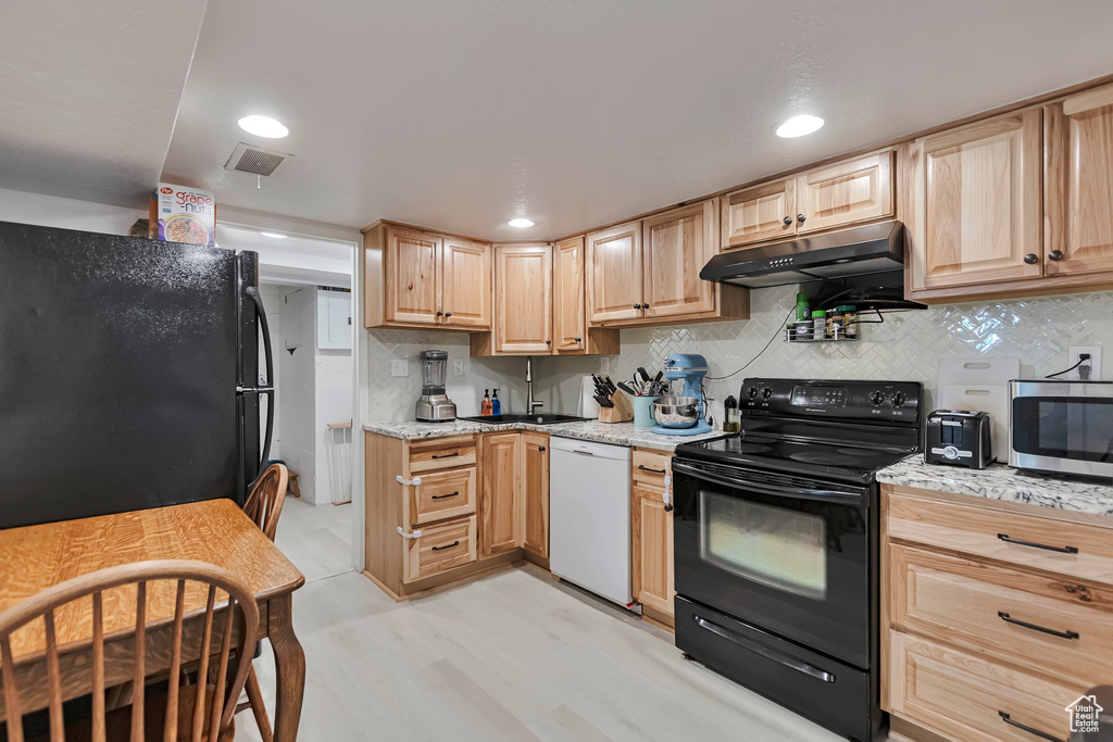 Kitchen with black appliances, under cabinet range hood, light brown cabinets, tasteful backsplash, and light stone countertops
