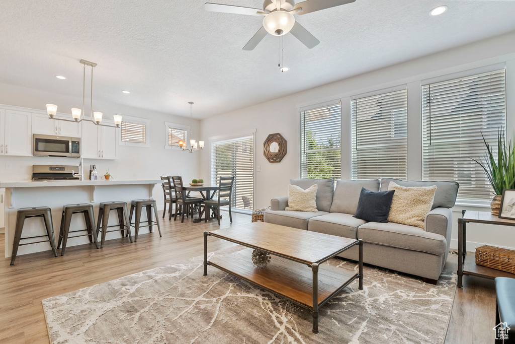 Living room featuring light wood finished floors, recessed lighting, a ceiling fan, a textured ceiling, and a chandelier