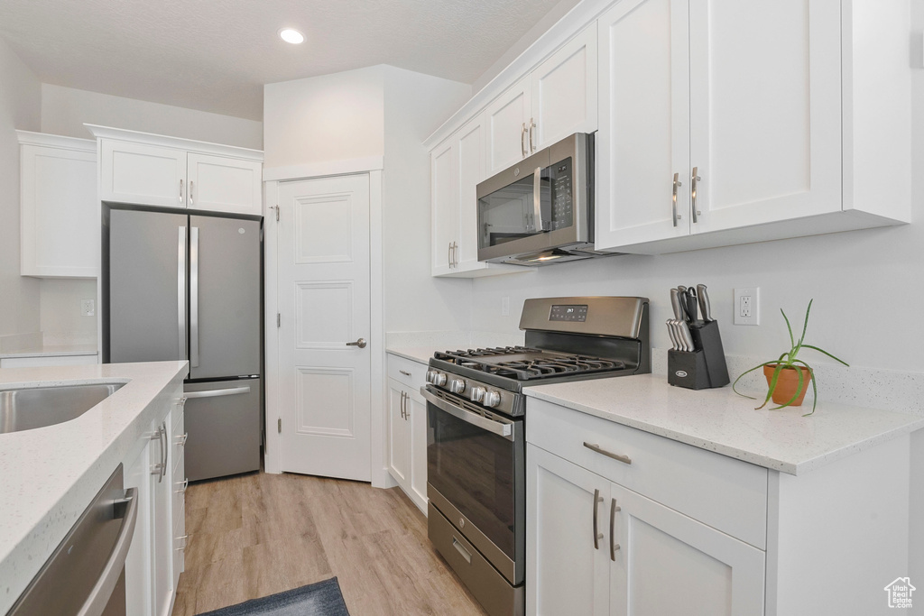 Kitchen with stainless steel appliances, white cabinetry, light wood-style flooring, recessed lighting, and light stone counters