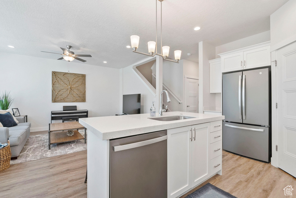 Kitchen with stainless steel appliances, open floor plan, light countertops, light wood-type flooring, and recessed lighting