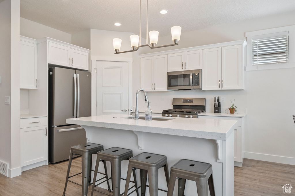 Kitchen featuring appliances with stainless steel finishes, white cabinetry, light wood finished floors, a kitchen bar, and recessed lighting
