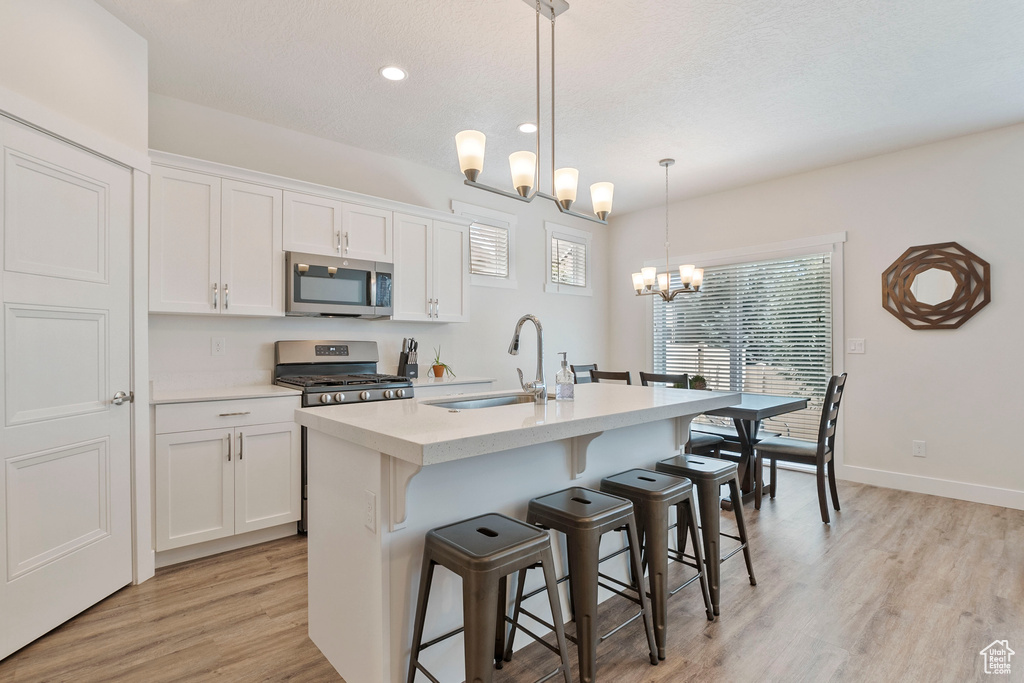 Kitchen with appliances with stainless steel finishes, a chandelier, light wood finished floors, an island with sink, and white cabinets