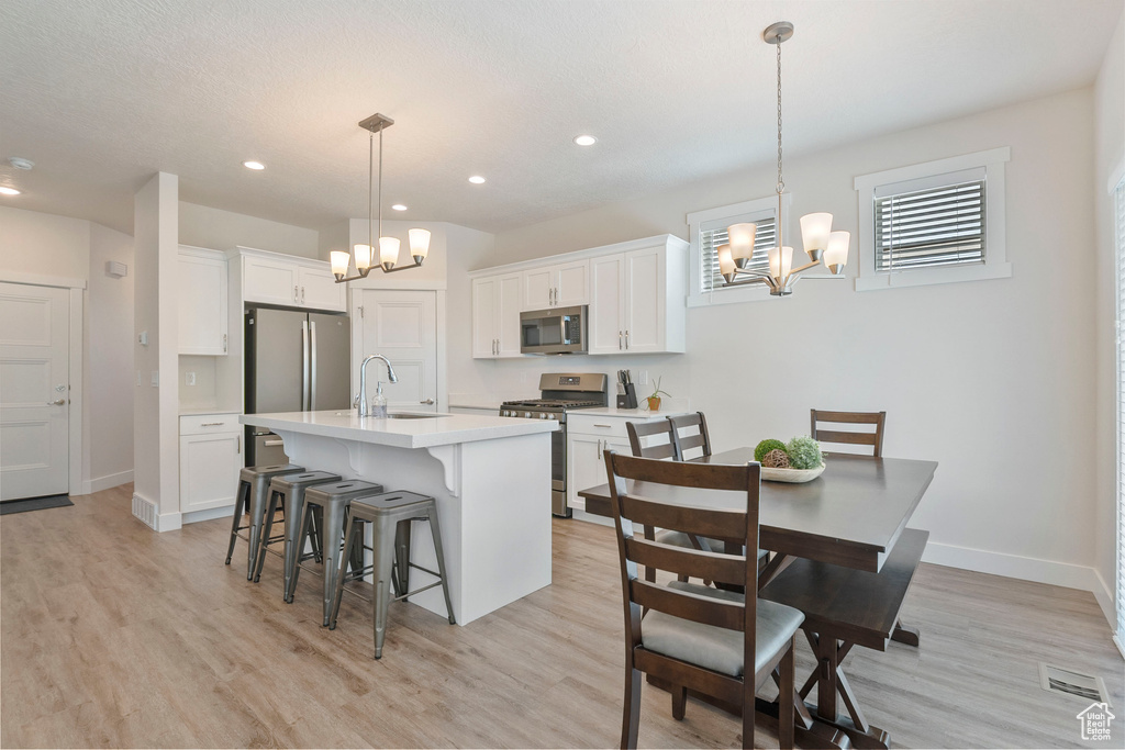Kitchen with stainless steel appliances, a chandelier, a kitchen breakfast bar, light countertops, and light wood-style flooring