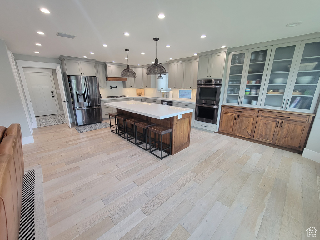 Kitchen featuring stainless steel appliances, a breakfast bar area, light countertops, light wood-type flooring, and a kitchen island