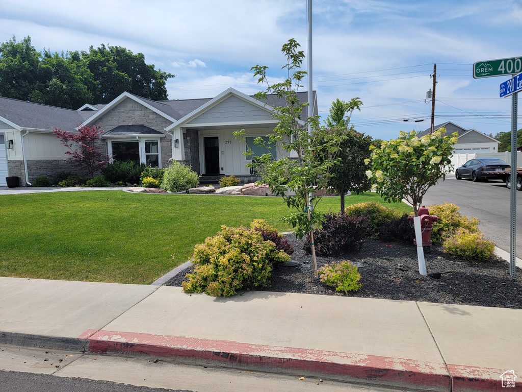 View of front of home with stone siding, a front yard, and covered porch