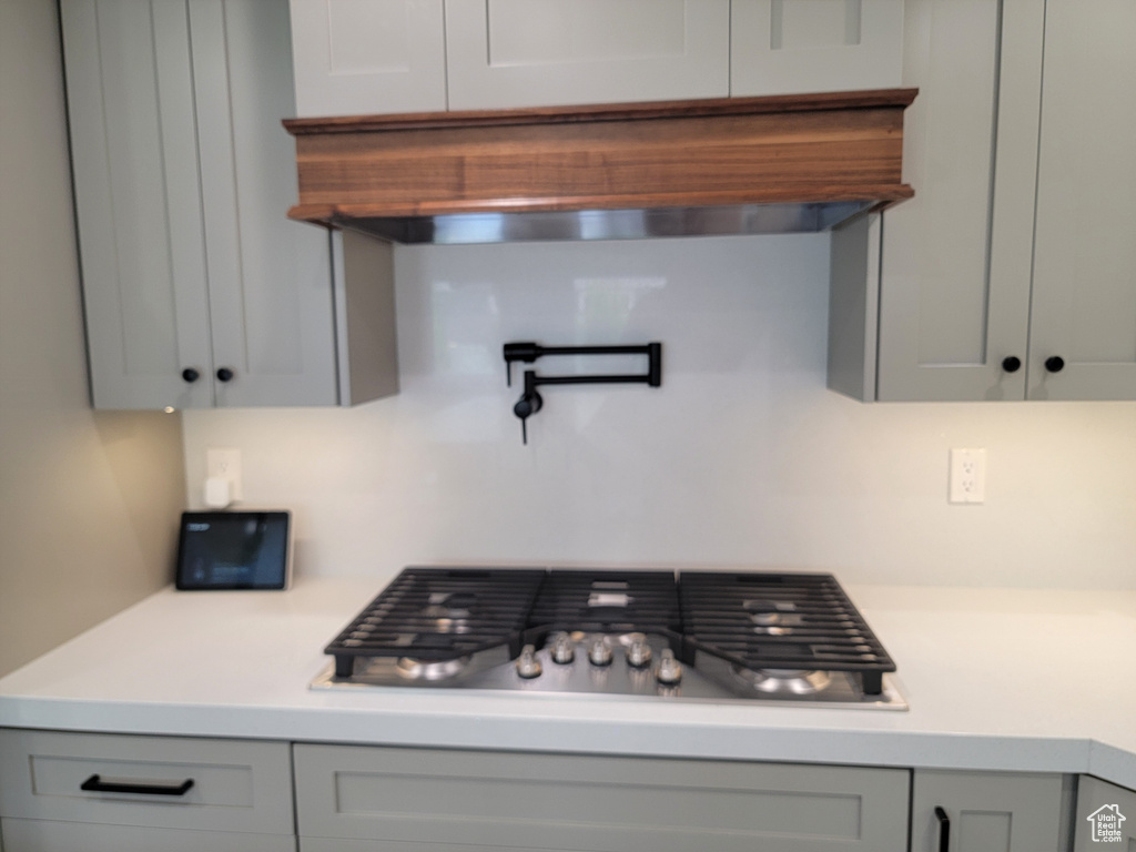Kitchen with stainless steel gas cooktop, light countertops, gray cabinets, and decorative backsplash
