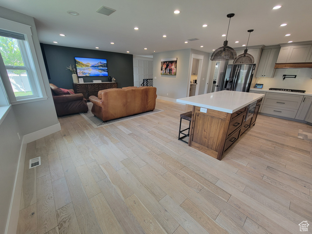 Kitchen featuring stainless steel refrigerator with ice dispenser, a kitchen bar, light wood-style floors, light countertops, and recessed lighting