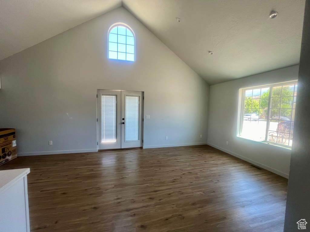 Unfurnished living room featuring dark wood finished floors, french doors, and high vaulted ceiling