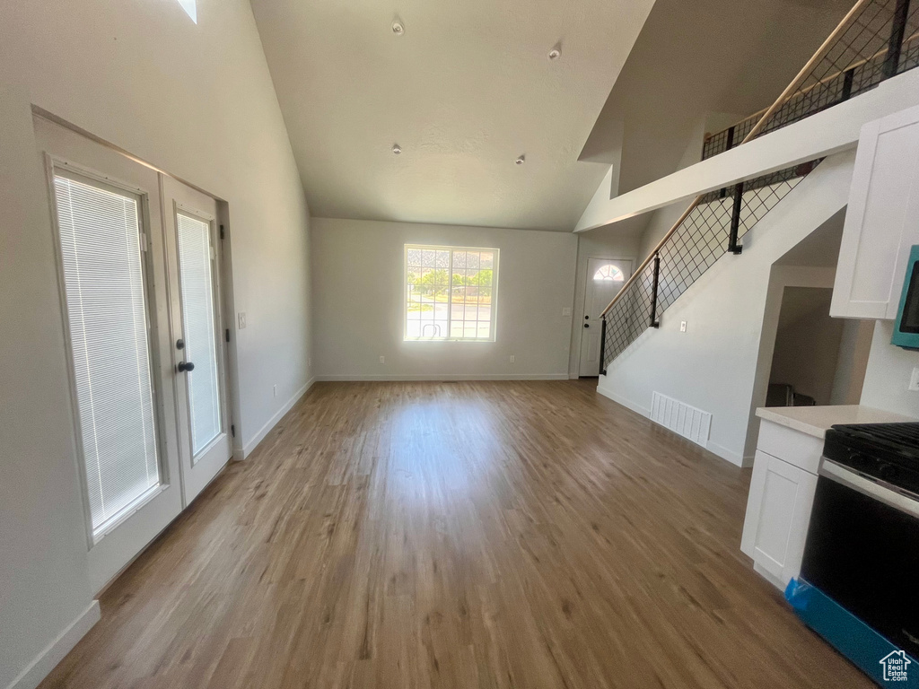 Unfurnished living room with high vaulted ceiling, light wood-style floors, and stairway