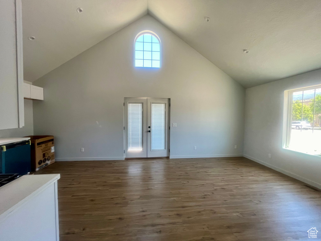 Unfurnished living room featuring plenty of natural light, wood finished floors, french doors, and high vaulted ceiling