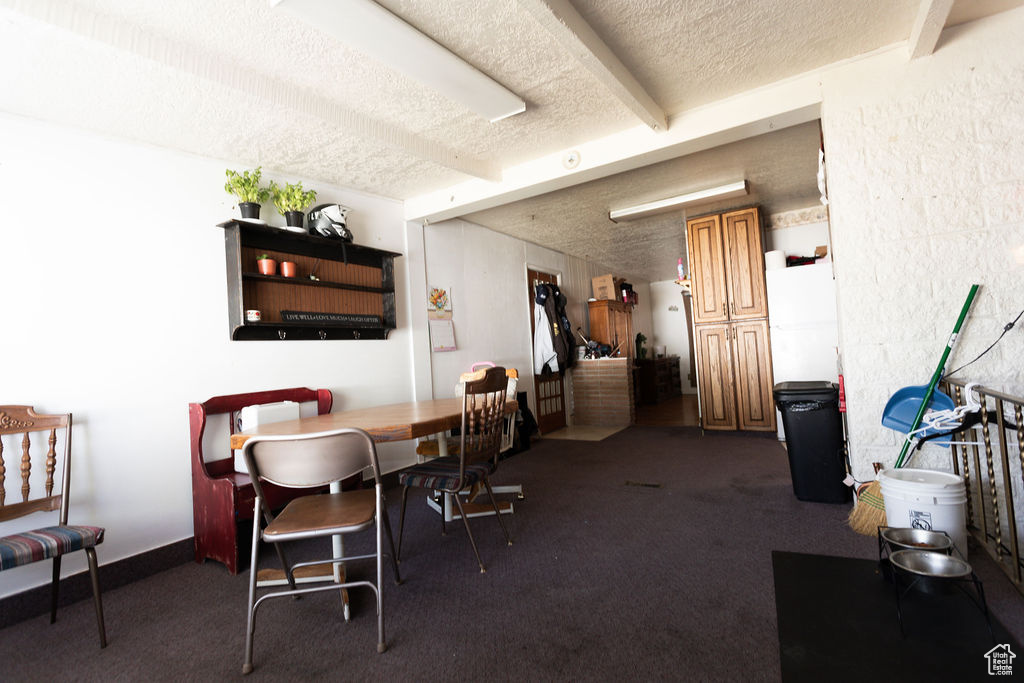 Dining room with a textured ceiling, beam ceiling, and dark colored carpet