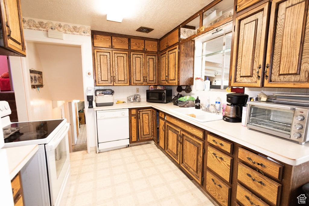 Kitchen with white appliances, brown cabinetry, light floors, light countertops, and a textured ceiling