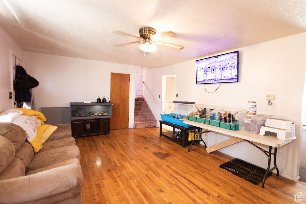 Living room with hardwood / wood-style floors, stairway, a ceiling fan, and a textured ceiling