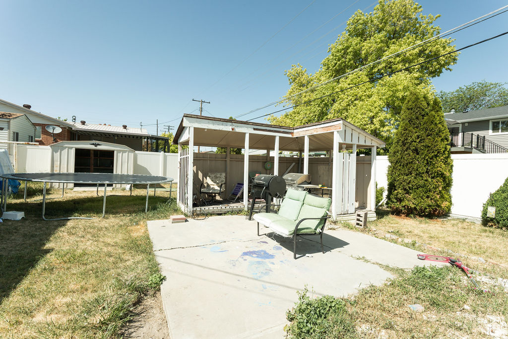 Fenced backyard featuring a trampoline and a patio area