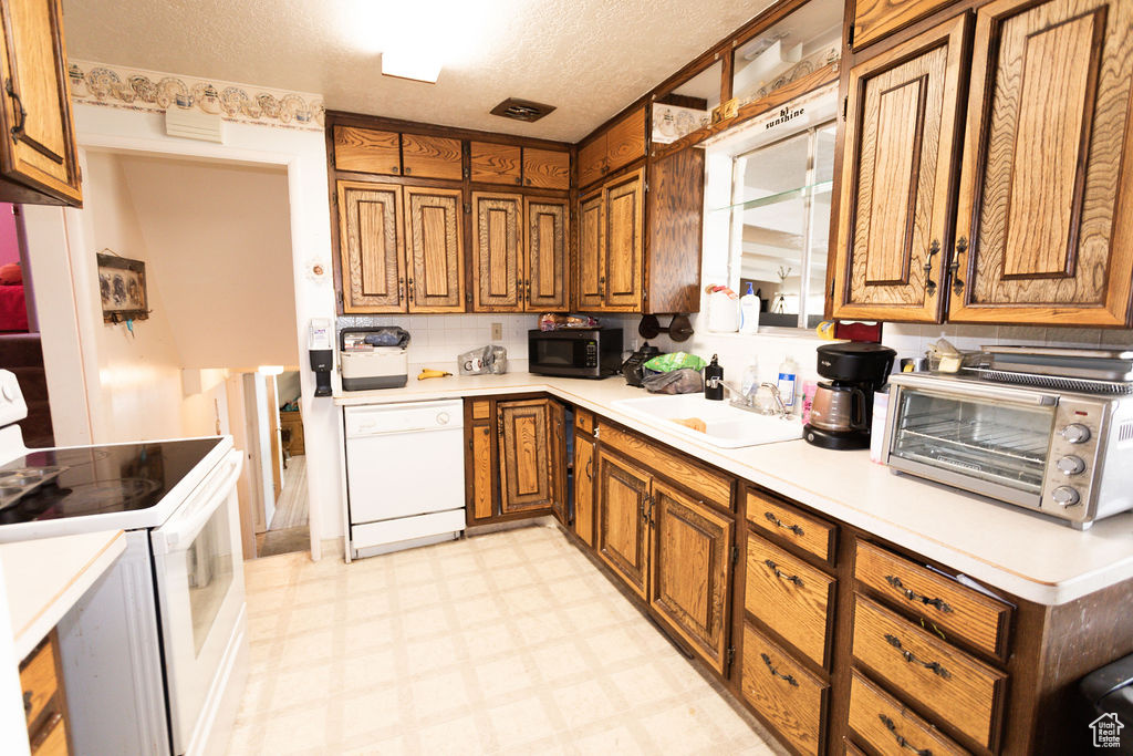 Kitchen with white appliances, brown cabinetry, light countertops, and a textured ceiling