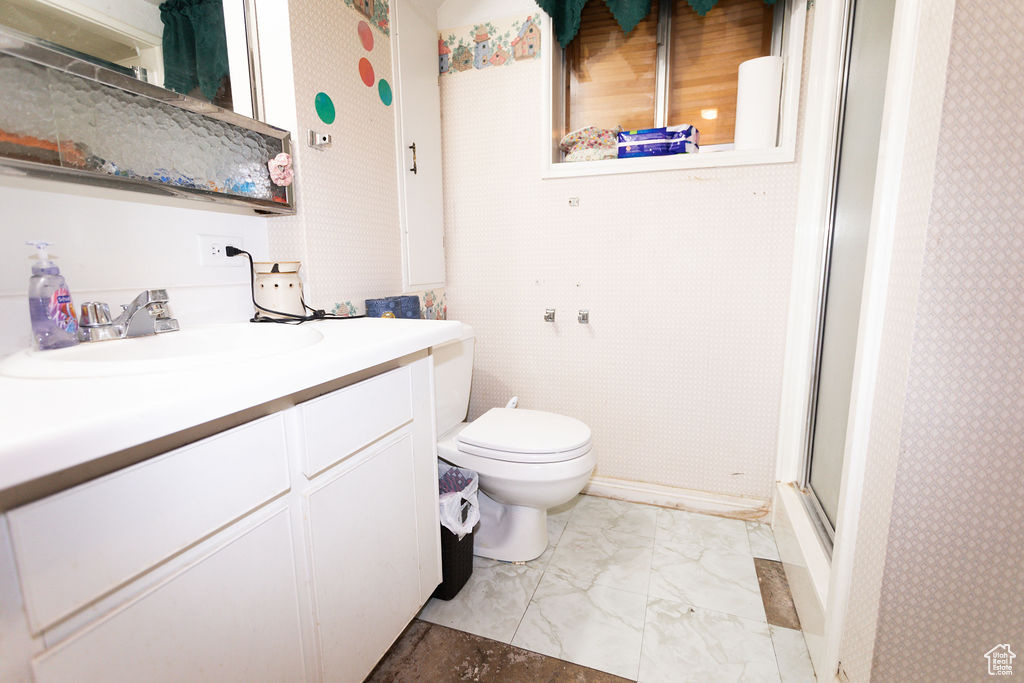 Bathroom with marble look tile flooring, vanity, a shower with door, and wallpapered walls